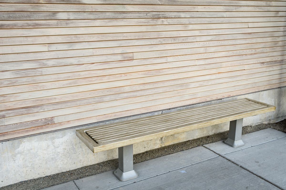 A wood bench against a textured wood wall on a concrete patio, a place to rest
